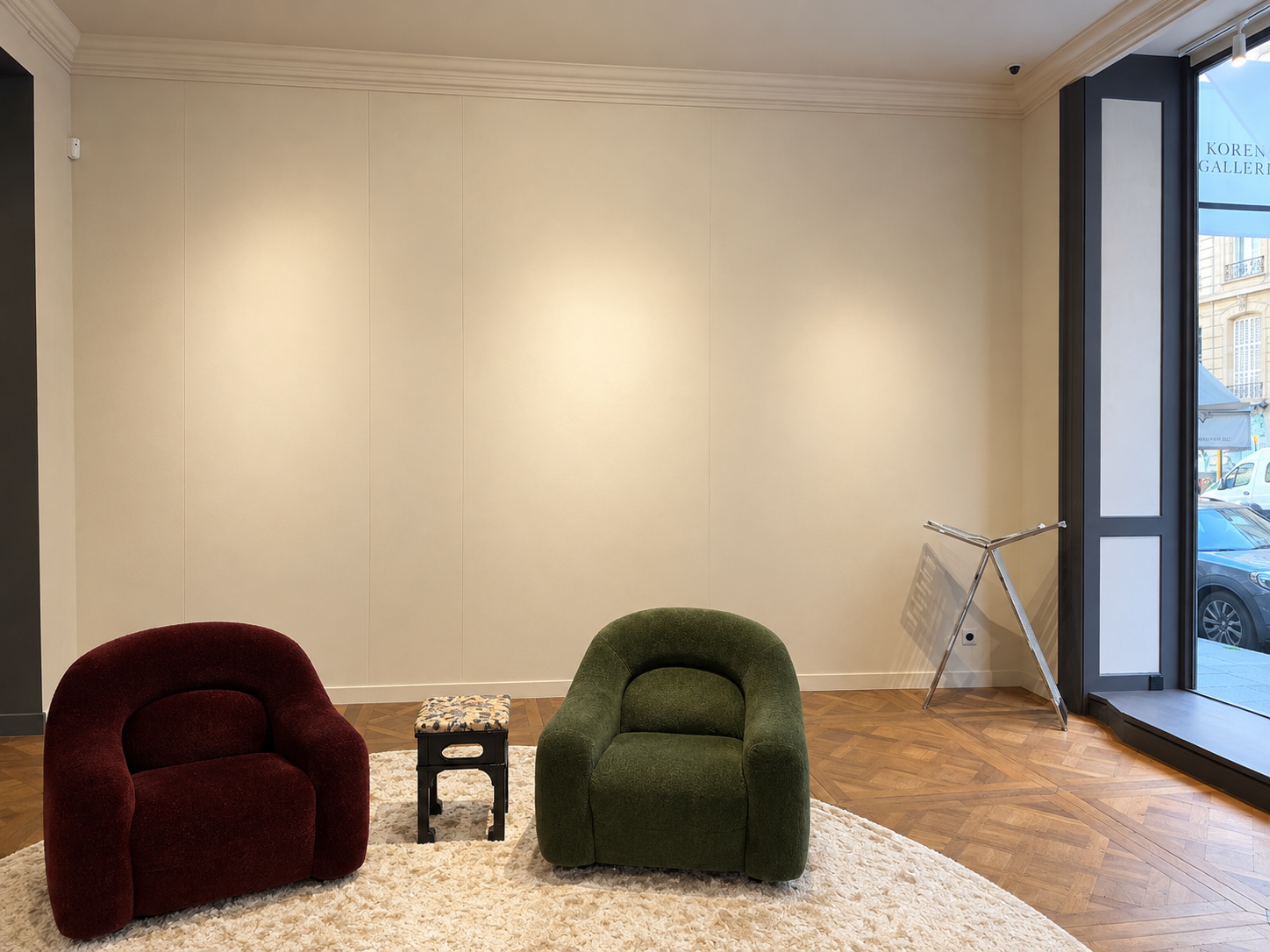 A seating corner with a burgundy and an olive armchair on a cream rug, walls left bare